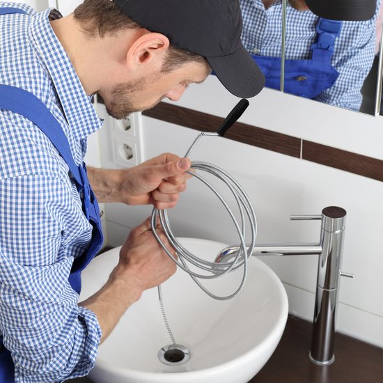 Monteur met ontstoppingsveer bij een wastafel.