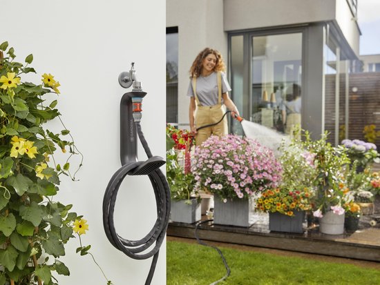 Vrouw met spuitmond op tuinslang, buiten bij bloemen en een opgerolde zwarte tuinslang aan een Gardena houder.