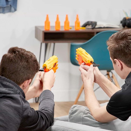 Twee jongens in grijze hoodies richten Nerf blasters op oranje flessen op een bureau.