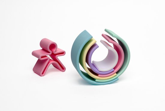Pastelkleurige regenboogvormen opgestapeld en een roze speelgoedfiguur in mensvorm, op een witte achtergrond.