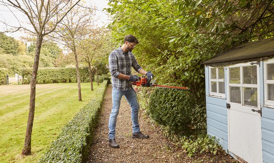Man met heggenschaar naast een blauw tuinhuisje.