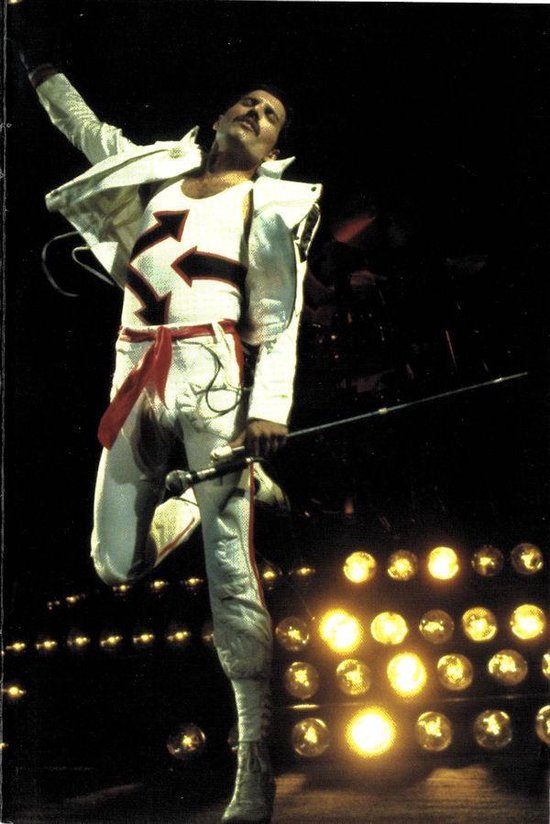 Freddie Mercury springt op podium in wit pak met rode accenten.