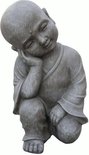 Statue de Bouddha enfant en pierre grise, assis en tailleur, tête sur la main.