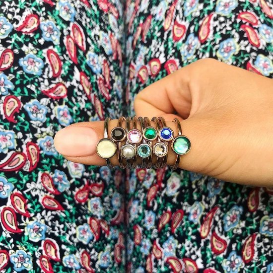 Hand met gekleurde ringen met edelstenen: geel, parel, blauw, groen, roze, wit.
