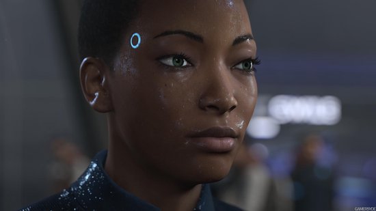 Close-up van het gezicht van een zwarte vrouw met kort zwart haar en groene ogen. Ze zweet en heeft een blauwe cirkel op haar voorhoofd.