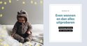 Baby in een bruin beren-pakje zit op een bed met lampjes.
