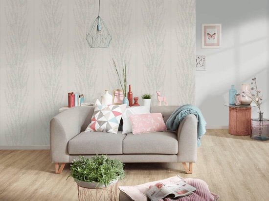 Een grijze tweepersoonsbank met kussens, plaid en planten staat voor een muur met verticaal bloesemdessin.