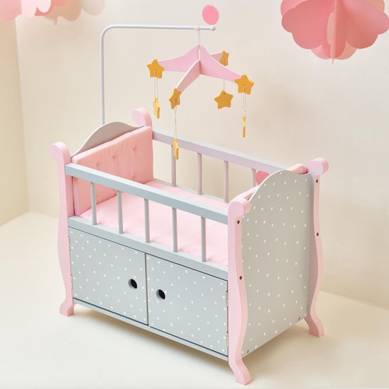 Roze poppenbedje met grijze zijkanten met witte stippen en twee opberglades aan de voorkant. Met sterrenmobiel.