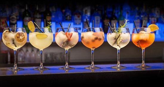 Zes gevulde cocktailglazen met diverse fruit garnituren en rietjes.