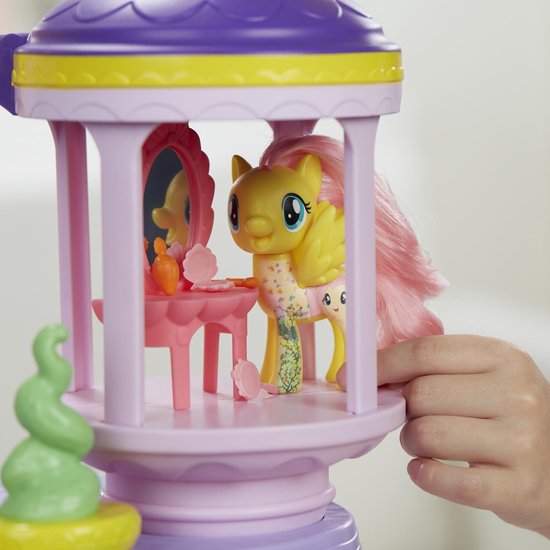 Gele Fluttershy pony met roze haar, vleugels en een tattoo, staand bij een roze spiegel en make-up.