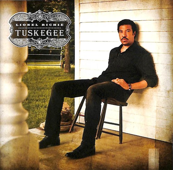 Lionel Richie in zwart overhemd en broek, zittend op een stoel buiten.