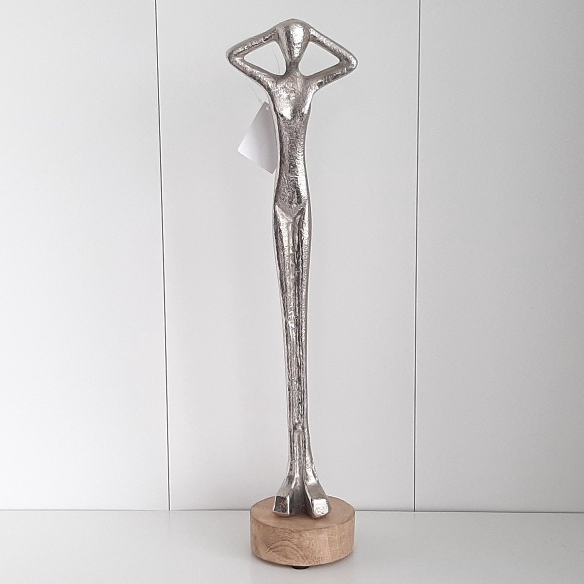 Zilverkleurig metalen beeld van een lang figuur met de handen op het hoofd, 37 cm hoog