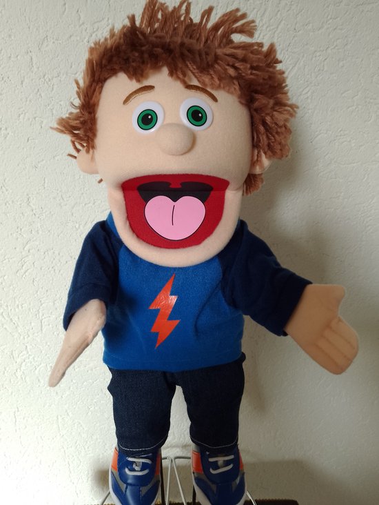 Handpop Tommie met bruin warrig haar, groene ogen en een grote open mond. Draagt een blauw shirt met oranje bliksemschicht, spijkerbroek en sneakers.