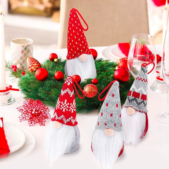 Décoration de table avec des nains de Noël portant des bonnets tricotés rouges et gris, dispersés parmi de la verdure et des boules de Noël.