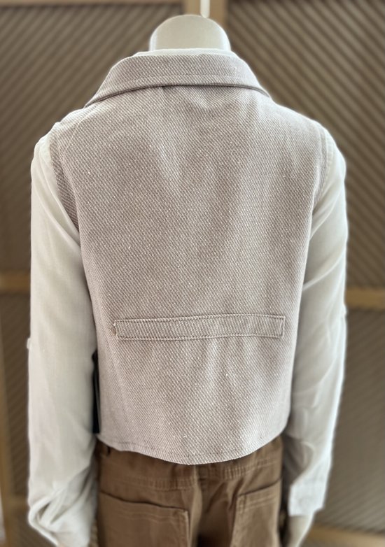 Achterkant van een beige vest en wit hemd, met bruine broek, gedragen door een mannequin.