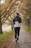 Vrouw met paardenstaart die jogt op een herfstachtig pad in een zwarte legging.