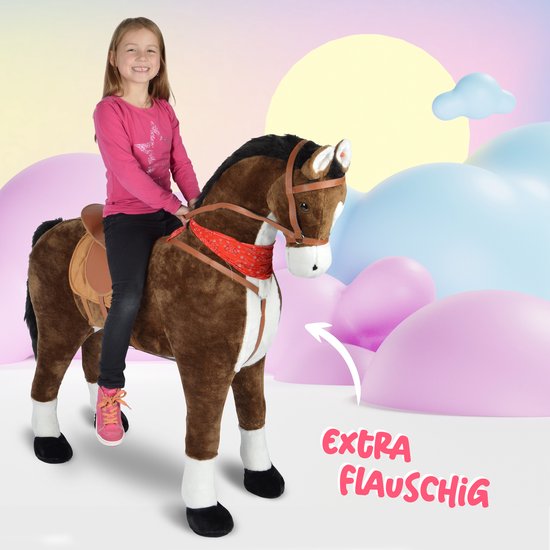 Meisje in roze shirt zittend op een bruin pluche paard met zadel en rode bandana, met zachte pastelkleurige achtergrond.
