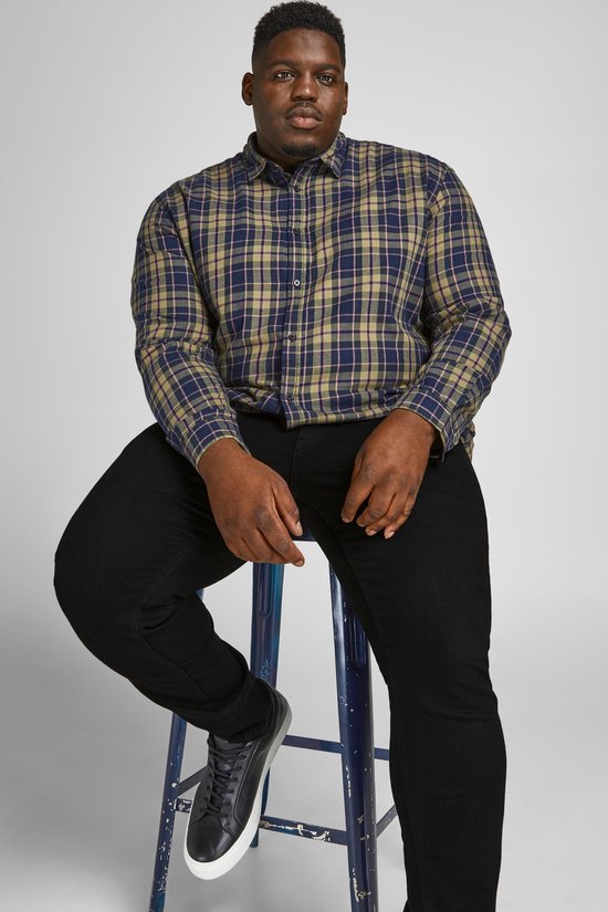 Man zittend op barkruk, draagt geruite blouse en zwarte jeans.