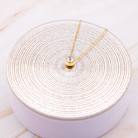 Gouden ketting met een enkele heldere zirkonia hanger, tentoongesteld op een zilveren spiraal display.