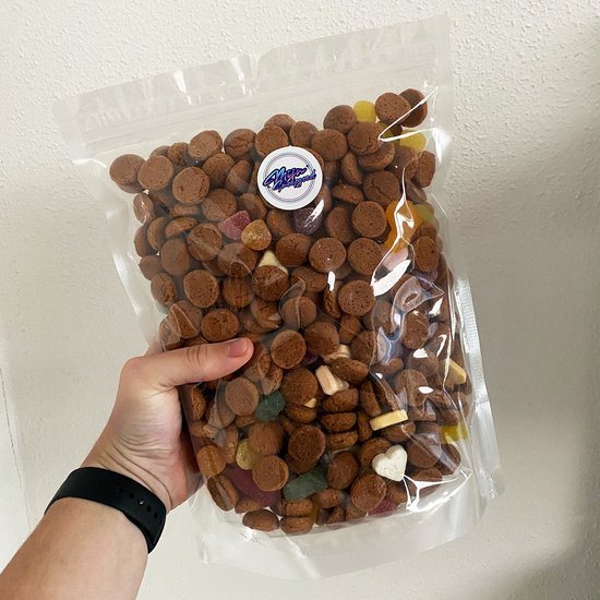 Een hand vult een grote zak met kruidnoten en speculaas. Mix van kruidnoten met gekleurde snoepjes.