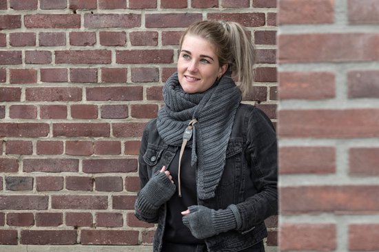 Model draagt een donkergrijze gebreide driehoekssjaal met een leren lipje.