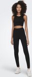 Model met zwarte crop top en nauwsluitende sportlegging met hoge taille en geribd patroon, en witte sneakers.