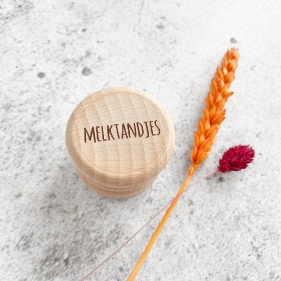 Houten bewaardoosje voor melktandjes met gegraveerde tekst, naast gedroogde bloemen.