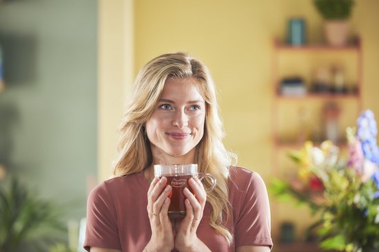 Een lachende blonde vrouw met een kop Pickwick thee in haar handen.