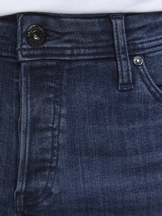 Detailopname van de blauwe spijkerbroek met knopen en stiksels.