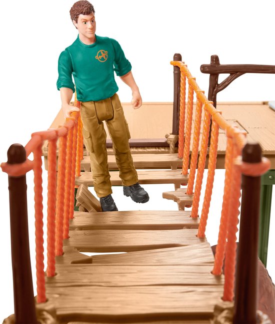 Verzorger die op een speelgoed hangbrug staat, met oranje touwen en houten planken.