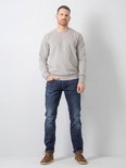 Man staat naar voren gericht, draagt een grijze trui en donkerblauwe jeans.