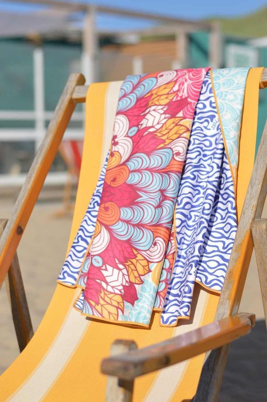 Strandlaken met kleurrijke mandala en blauwe golven print, liggend op een gele gestreepte ligstoel op het strand.
