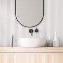 Moderne badkamer met een stenen wastafel en een ronde spiegel. Een RVS zeeppompje staat op een houten meubel.