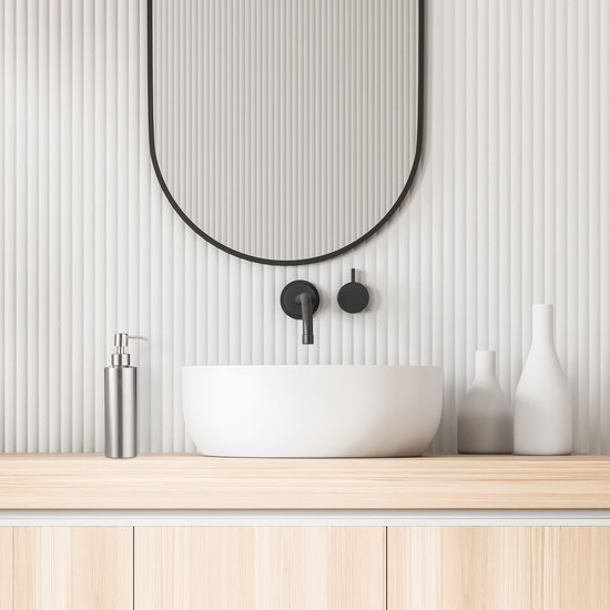 Moderne badkamer met een stenen wastafel en een ronde spiegel. Een RVS zeeppompje staat op een houten meubel.