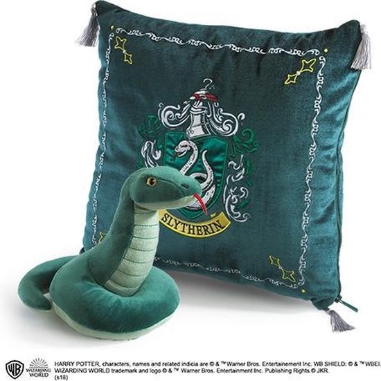 Serpent en peluche vert à côté d'un coussin décoratif vert foncé arborant les armoiries de Slytherin et des glands.