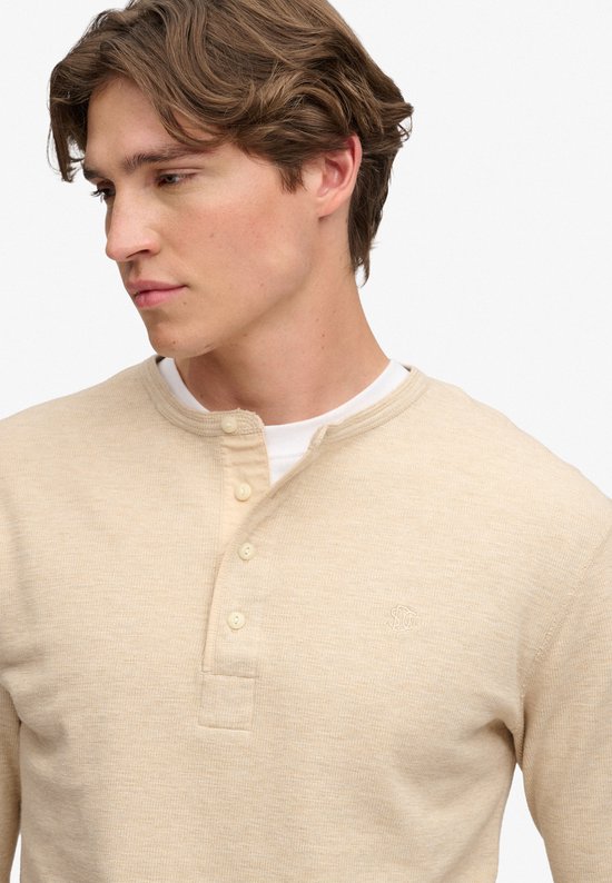 Close-up van het model in een beige waffle grandad-top met knoopsluiting over een wit T-shirt.