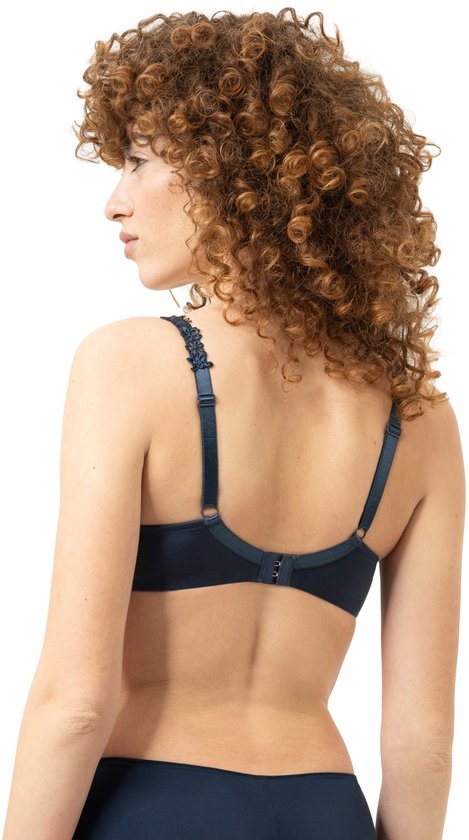 Model met krullend bruin haar, van achteren gezien, draagt een marineblauwe beugelbeha.