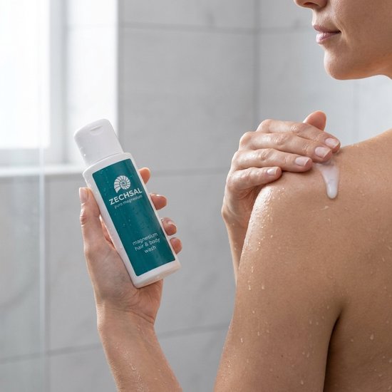 Vrouw in de douche die Zechsal magnesium hair & body wash op haar schouder aanbrengt.