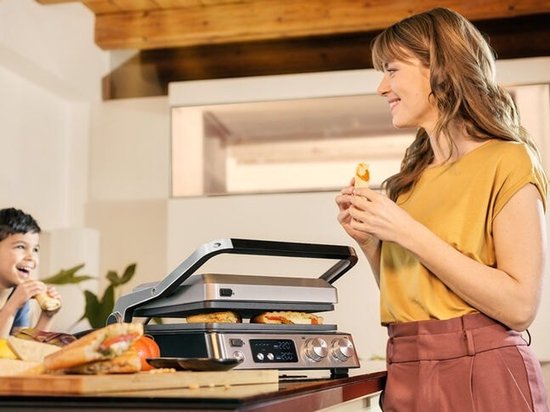 Man en vrouw bij open wafelijzer/contactgrill, vrouw giet stroop op wafels.