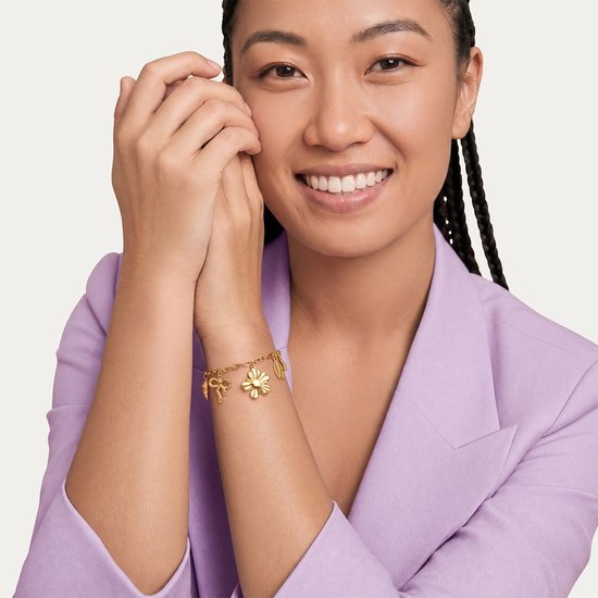 Gouden bedelarmband met strik, bloem en veer aan een dame met vlechten.
