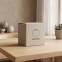 Bruine Nore verpakking met logo van een kom, op een houten tafel.