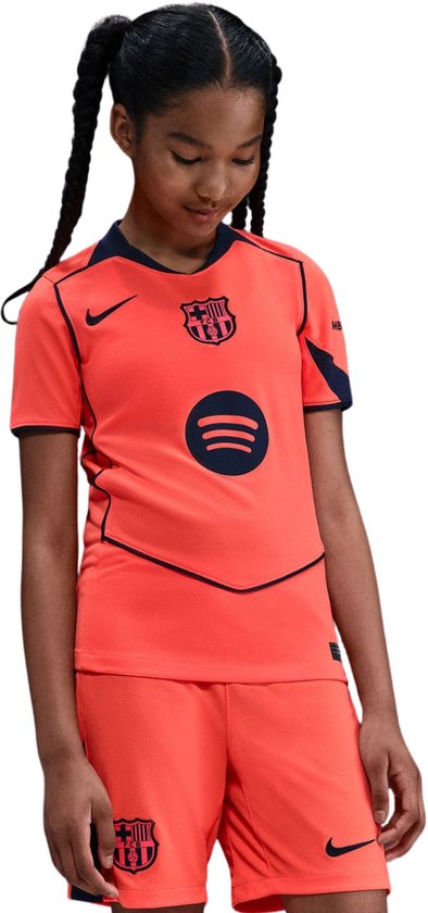 Oranje Nike T-shirt van FC Barcelona met donkerblauwe accenten en het Spotify logo op de voorkant. Een meisje met gevlochten haar draagt het shirt.