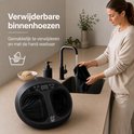 Vrouw wast verwijderbare hoes van zwart voetmassageapparaat in gootsteen.