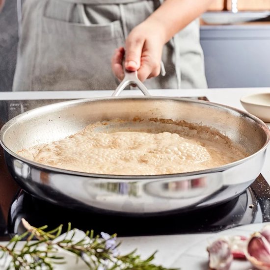 Bodem van een roestvrijstalen pan, met suddelende saus en belletjes, op een kookplaat.