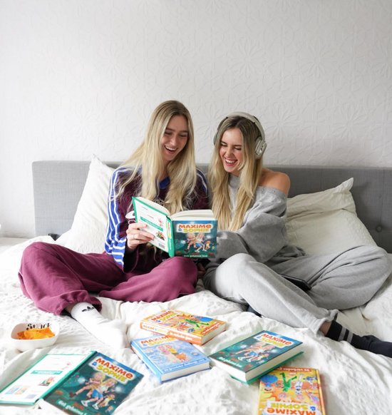 Twee lachende jonge vrouwen zitten op een bed met de boeken 'Maxime & Sophie - Het geheime bos'.