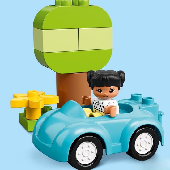 Blauwe LEGO Duplo auto met een meisje met zwarte staartjes erin, naast een boom met een gele bloem.