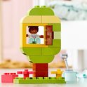 Arbre vert avec porte et fenêtre jaunes, avec une fille à l'intérieur. À côté d'un petit jardin avec des outils.
