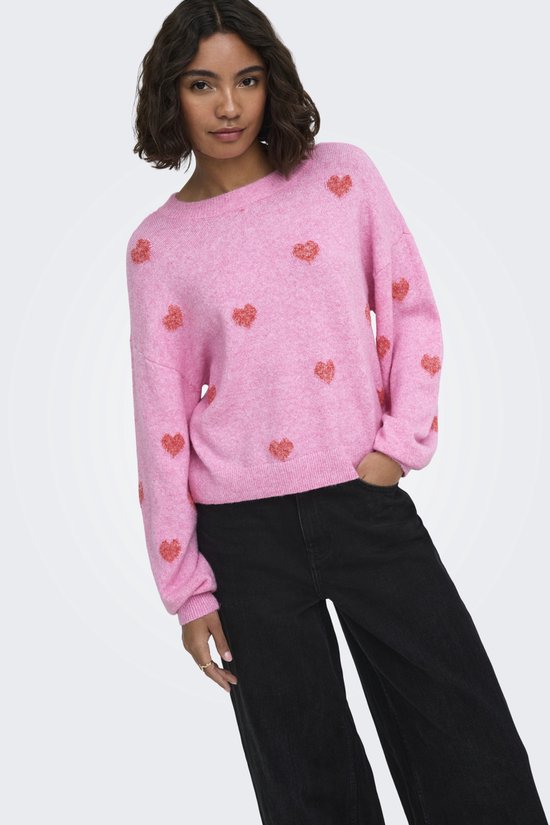 Model draagt roze trui met rode hartjesprint, lange mouwen en ronde hals, met zwarte broek.