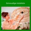 Een vrouw met rood haar installeert een rieten hanglamp.