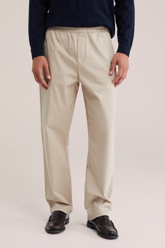 Man draagt een beige wijde broek met elastische tailleband en steekzakken.